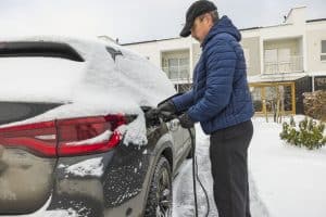 Beautiful view of a man connecting a charging cable to an electric car charging station on a frosty winter day.