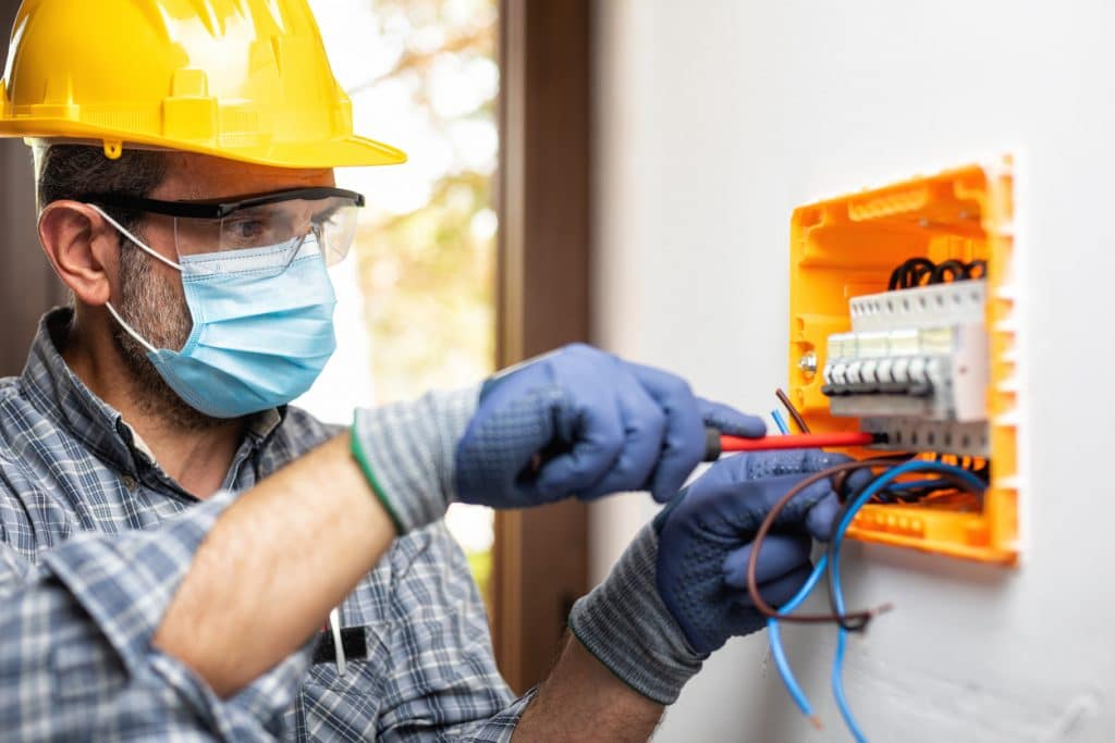 Electrician at work on an electrical panel protected by helmet, safety goggles and gloves; wear the surgical mask