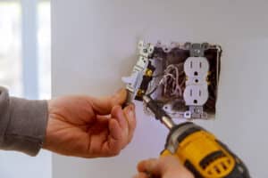 The hands of an electrician installing a power switch to the electrical junction box